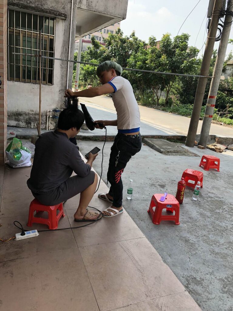 A young man gives another young man a haircut on an outdoor patio